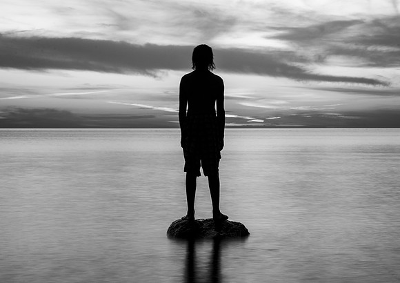 Lone Boy Standing on Rock in Lake